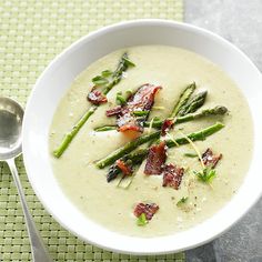 a bowl of soup with asparagus and bacon in it on a green place mat