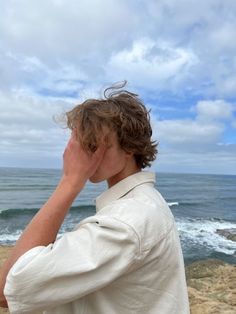 a man standing on top of a sandy beach next to the ocean holding his head