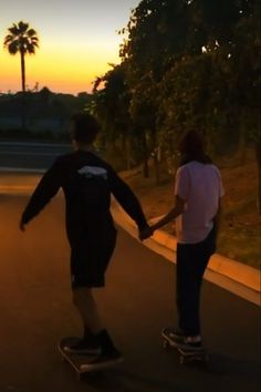 two people are skateboarding down the street at sunset