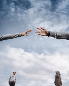 two men reaching out their hands to reach something in the sky with clouds behind them