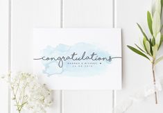 congratulations card with watercolor paint and greenery on white wooden background next to flowers