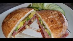 a sandwich cut in half sitting on top of a white plate next to cucumbers