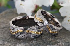 two wedding rings sitting on top of a rock with flowers in the backgroud