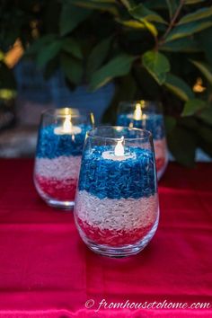 red, white and blue candles are sitting in glass vases on a tablecloth