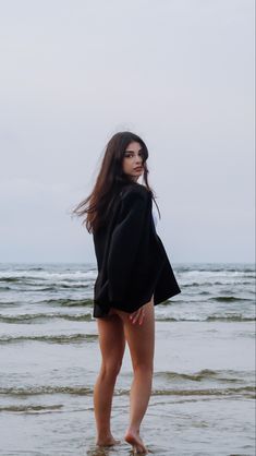 a woman standing in the water at the beach with her back turned to the camera