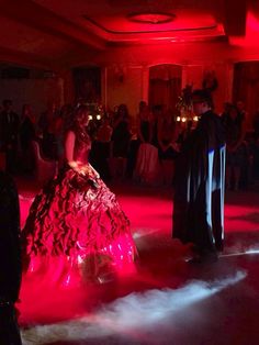 two people dressed in formal wear standing on a dance floor with red lights behind them