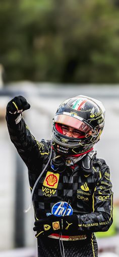 a man wearing a helmet and holding his hand up in the air while standing on top of a race track