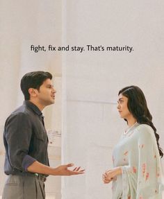 a man and woman standing next to each other in front of a wall with words on it