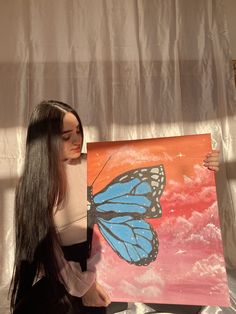 a woman sitting on the ground holding up a painting with a blue butterfly on it