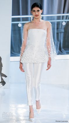 a model walks down the runway wearing white clothing with sheer sleeves and pearls on her head