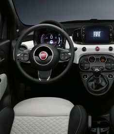 the interior of a small car with white leather and black trims, steering wheel