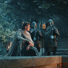 a man sitting on top of a stone wall next to other men wearing armor and helmets