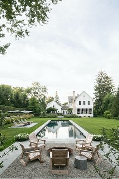 an outdoor fire pit with chairs around it and a house in the background, surrounded by greenery