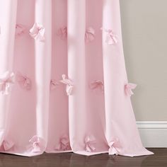 a pink curtain with bows on it in front of a white wall and hardwood floor