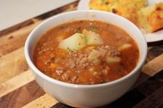 a white bowl filled with soup sitting on top of a wooden table next to a piece of bread