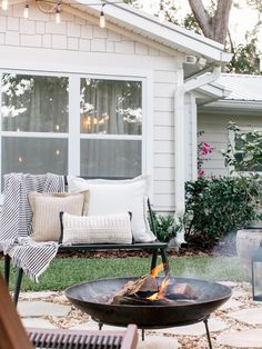 a fire pit sitting in the middle of a yard next to a house with pillows on it