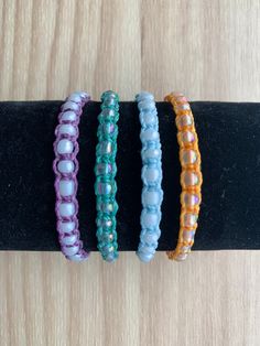 three bracelets are sitting on top of a black piece of wood and one is made out of glass beads