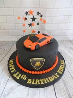 a birthday cake with a car and stars on the top is decorated in black, orange and gold