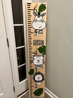 a wooden growth chart with animals on it in front of a door that says hudson