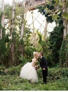 a bride and groom kissing in the woods