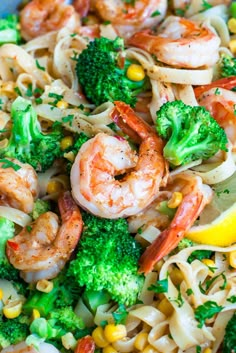 shrimp, broccoli and noodles with lemon wedges on a white plate topped with corn