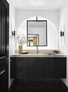 a black and white bathroom with an arched mirror above the sink, along with a vase filled with flowers