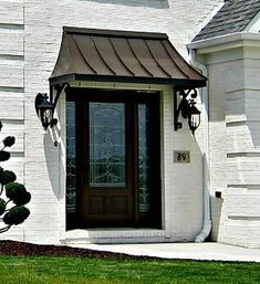 the front door of a white brick house with a brown metal awning over it