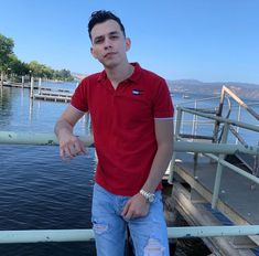 a man standing on a pier next to the water with his hand in his pocket