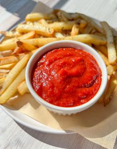 a white plate topped with fries and ketchup on top of a wooden table