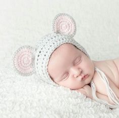 a newborn baby wearing a crocheted mouse hat sleeping on a white blanket with its eyes closed