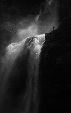 a man standing on top of a waterfall in the middle of black and white photo