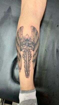 a man's leg with a tattoo on it that has wings and a cross in the middle