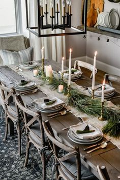 a dining room table set for christmas with candles and greenery on the long table