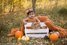 a baby sitting in a wooden crate surrounded by pumpkins and other fall decorations,