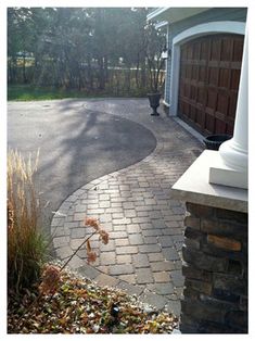 a brick driveway with a white column in the middle and a brown garage door behind it