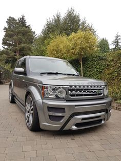 a silver range rover is parked in front of some bushes and trees on a brick walkway