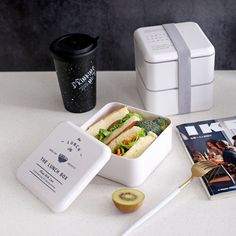 the lunch box is next to two coffee mugs and a magazine on the table