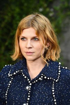 a woman with blonde hair wearing a blue jacket and pearls on her collar is looking at the camera