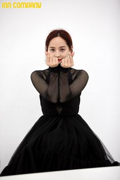 a woman in a black dress with her hands on her face, posing for the camera