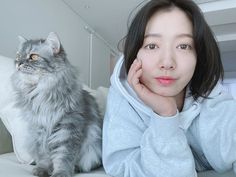 a woman laying on top of a bed next to a gray and white cat in front of her