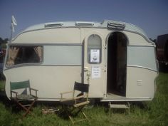 an old camper is parked in the grass with two lawn chairs next to it