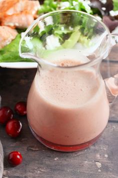 a glass pitcher filled with liquid next to a plate of salad and cherries on the table