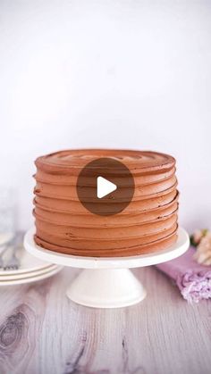 a chocolate cake sitting on top of a white cake plate next to a pink flower