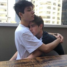 two young men hugging each other at a table in front of a cityscape