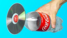 a hand holding a can of coca - cola in front of a cd disc on a blue background