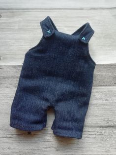 a baby's denim romper with buttons on the front and back, sitting on a wooden floor