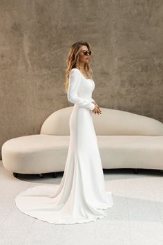 a woman standing in front of a white couch wearing sunglasses and a long sleeved dress