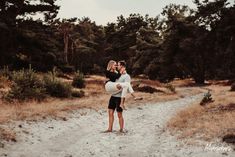 a man carrying a woman on his back in the middle of a dirt road surrounded by trees