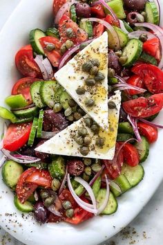 a white plate topped with cucumber, tomatoes and olives