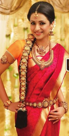 a woman in a red and gold sari with her hands on her hips, smiling at the camera